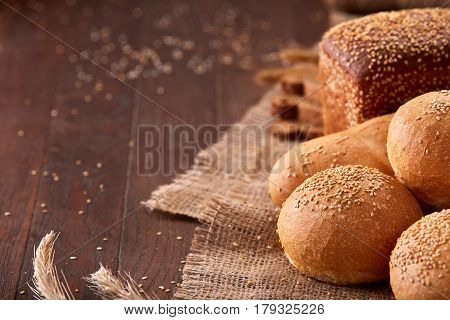 Different bread on burlap on the wooden table close-up. With wheat and ears of wheat. Slices of the brown bread. Rulls and baguette.