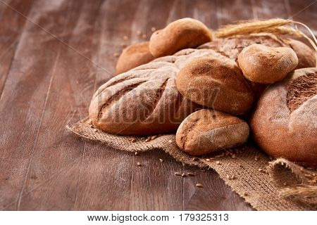 handmade tasty bread lying on burlap on the wooden table with flour, wheat and ears of wheat. Brown bread and rulls. Delicious food. Fresh baking. Tasty and appetizing.
