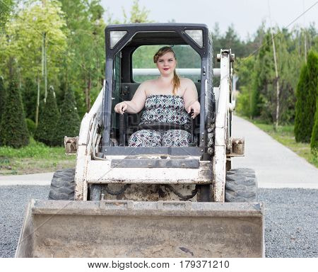 A beautiful girl plus size manages a tractor in a garden nursery