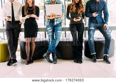 Close Up Of Group Of Friends Standing On Table And Browsing In Their Divices In Modern Room. Togethe