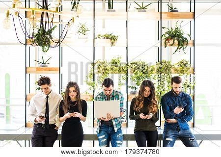 Group Of Friends Standing On Table And Everyone Use His Divices In Modern Office Room. Together Fun