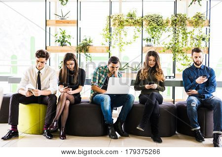 Group Of Friends Sitting On Chairs Near Each Other And Everyone Use His Divices In Modern Office Roo