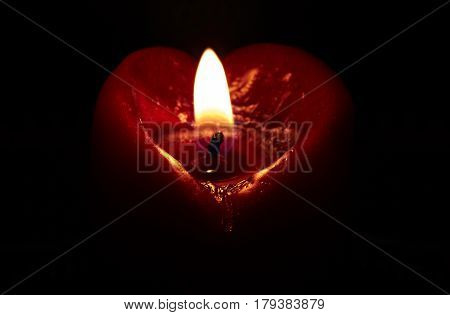 Candle that has a heart shape burns on a black background