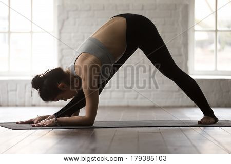 Young sporty yogi woman practicing yoga concept, stretching in One Sided Fold, Ardha Parsvottanasana exercise, Half Pyramid pose, working out, wearing black sportswear, full length, white loft studio