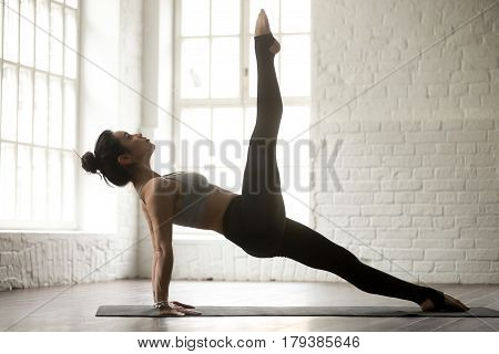 Young attractive yogi woman practicing yoga concept, standing in Purvottanasana exercise, One legged Upward Plank pose, working out, wearing sportswear, full length, white studio background, side view