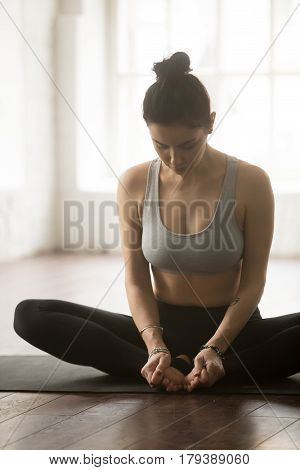 Young attractive yogi woman practicing yoga concept, sitting in baddha konasana exercise, Butterfly pose, working out, wearing sportswear bra and pants, white loft studio background, vertical
