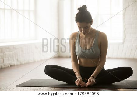 Young attractive sporty yogi woman practicing yoga concept, sitting in baddha konasana exercise, Butterfly pose, working out wearing sportswear bra and pants, full length, white loft studio background