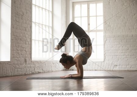 Silhouette of young cool attractive yogi woman practicing yoga concept, doing vrischikasana exercise, Scorpion pose, working out, wearing black sportswear, full length, white loft studio background