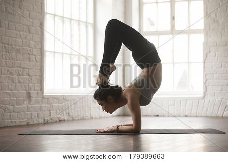 Silhouette of young cool yogi woman practicing yoga concept, stretching in vrischikasana exercise, Scorpion pose, working out, wearing black sportswear pants, full length, white loft studio background