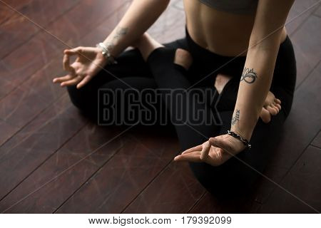 Young yogi woman with tattoo practicing yoga, sitting on floor in Padmasana, Lotus pose, working out wearing sportswear pants, horizontal photo. Indoor. Meditation session concept. Midsection close up