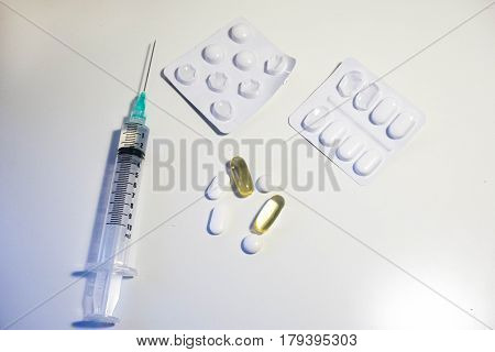 A variety of medication including a syringe with a green tip two blister packs white pills and yellow plastic pills full of cod liver oil vitamin D supplement against a white background