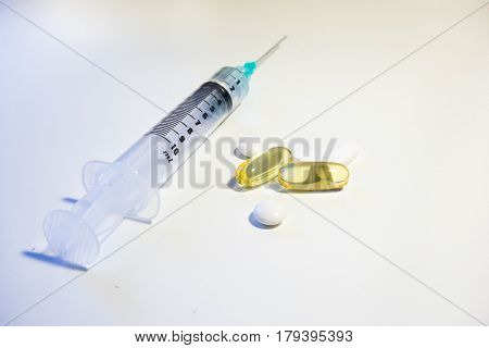 Syringe with green tip containing clear fluid and white and yellow pills containing cod liver oil vitamin D supplement at a low angle against a white background