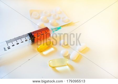 A syinge containing 4ml of red fluid sits next white and yellow pills and a blister pack from close up