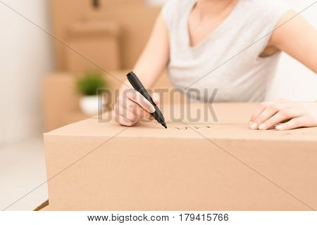 Young woman signs a box while moving. Cleaning and packing. The concept of move.