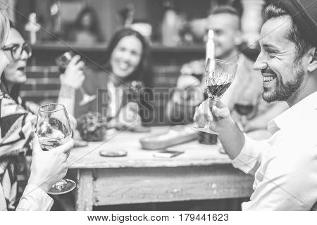 Happy fashion friends toasting wine in trendy cocktail bar restaurant - Young people having fun drinking and laughing together - Focus on right man mouth eye - Black and white editing - Warm filter