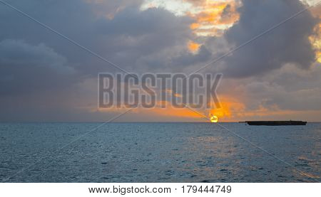 Shadow of a barge at sea when the blazing orange sun touches the bleu Carribean water.
