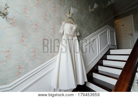 Cream bride dress hang on the lamp against the wall next to the stairs in the hotel