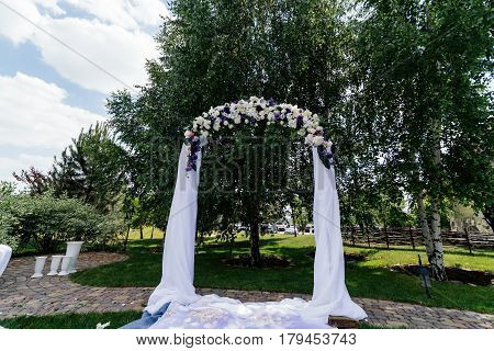 Wedding arch with flowers and white cloth near the birch