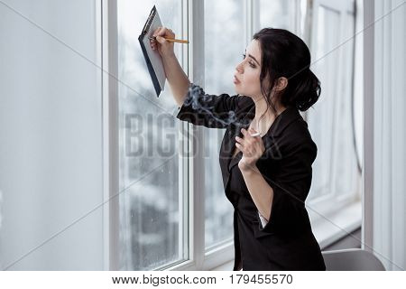 Business woman in office with a cigarette makes notes in notepad