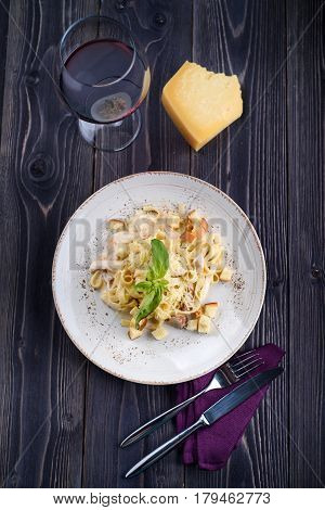 Pasta with meat and mushrooms on a white plate and a glass of wine