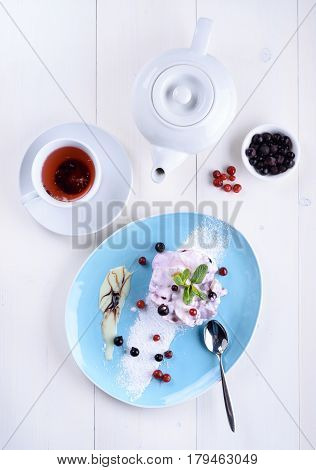 Cake with fresh berries on a blue plate next to a cup of tea and a teapot. Berry cake with tea