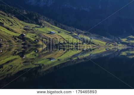 Green farmland mirroring in lake Wagital Swiss Alps.