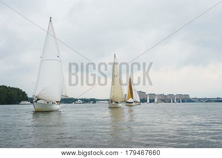 Sailing, yachting. Walk on a sailing yacht on the pond, the lake, on a cloudy summer day. Several large white sailing boat during the boat ride, or regatta. Summer vacation on the beach.