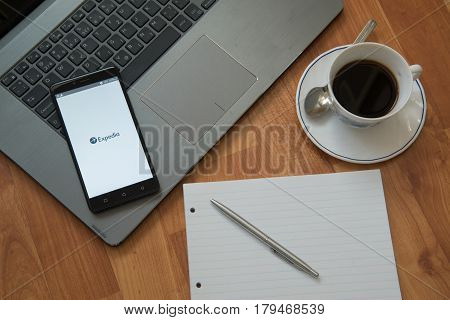 Nitra, Slovakia, march 28, 2017: Expedia application in a mobile phone screen. Workplace with a laptop, an earphones, notepad, pen and coffee on wooden background