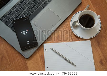 Nitra, Slovakia, march 28, 2017: TomTom Go application in a mobile phone screen. Workplace with a laptop, an earphones, notepad, pen and coffee on wooden background