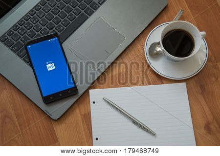 Nitra, Slovakia, march 28, 2017: Microsoft Office Word application in a mobile phone screen. Workplace with a laptop, an earphones, notepad, pen and coffee on wooden background