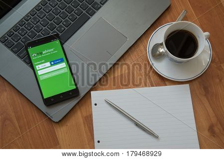 Nitra, Slovakia, march 28, 2017: Tripadvisor application in a mobile phone screen. Workplace with a laptop, an earphones, notepad, pen and coffee on wooden background