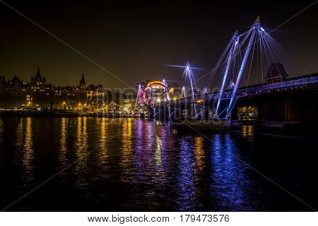 Hungerford Bridge and Golden Jubilee Bridges  and Whitehall Gardens at night with lights reflected in Thames water , London