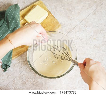 Top view of the dough and ingredients for making traditional thin pancakes. The process of cooking pancakes for breakfast. Hands girls whisking dough. Soft focus.