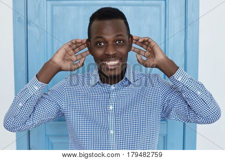 Headshot of bug-eyed young African man grimacing looking at camera with funny face expression clowning and having fun indoors pulls his ears fooling around and indulge.