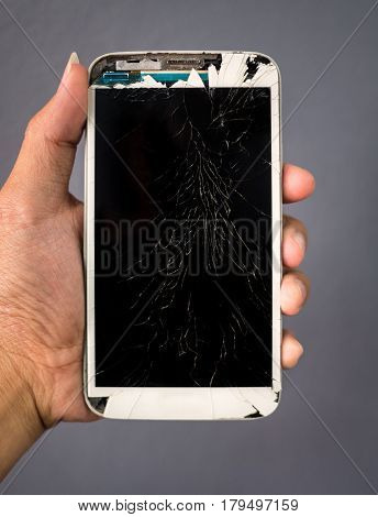 Human hand holding broken cracked screen smartphone on gray background