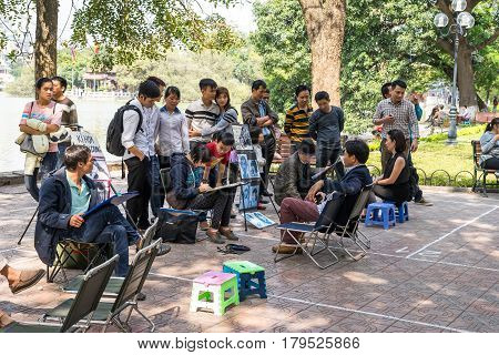 Hanoi Vietnam - February 17 2016: Asian portrait painter drawing sketch of customer by pencil on the sidewalk of Hoan Kiem lake in Hanoi Vietnam