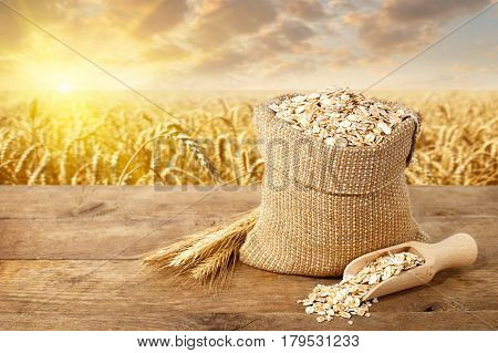Oat flakes in sack. Ears of oats and oatmeal in bag on table with ripe cereal field on the background. Agriculture and harvest concept. Uncooked porridge. Golden field on sunset