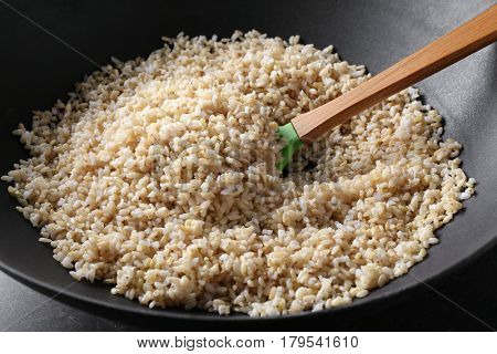 Wok full of brown rice with wooden stirring spoon