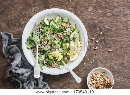Quinoa and greens veggies salad for a spring detox. Salad with quinoa cucumbers avocado arugula ginger flax seeds and nuts on wooden background top view. Mediterranean style food concept