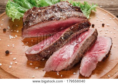 Thick slices of superior grilled beef steak decorated with lettuce leaf, served on wooden table, close up view. American food. Menu photo.