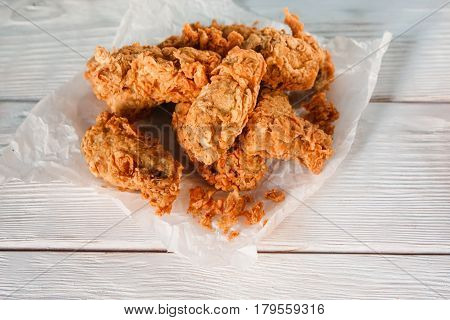 Fresh deep fried chicken in paper on white wooden table, flat lay. American cuisine, junk food, bad habits, calories, cholesterol, fatness.