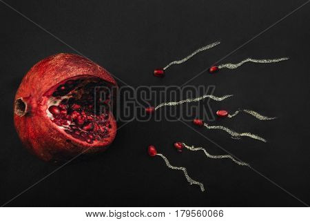 Pomegranate with juicy seeds on black background, flat lay. Symbol of female egg and sperm, ovulation, sex, woman fertility concept.