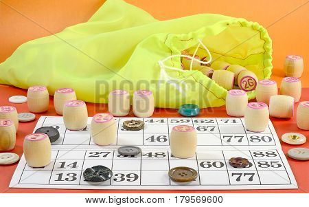 photo side view of details of Russian vintage game Bingo or Lotto with white paper cards in the cells which contain numbers small wooden barrel on which is written the numbers green bag multi-colored buttons on the table red color