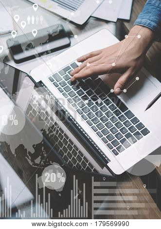 Businessman working at sunny office on laptop while sitting at the wooden table.Concept of digital screen, virtual connection icon, diagram, graph interfaces on background.Blurred, vertical