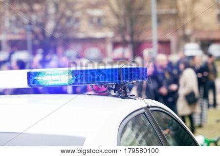 Police car flashing lights in focus, blurred crowd in background