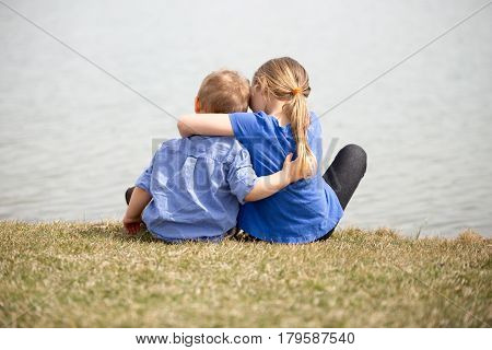 Young sibling boy and girl looking at the lake holding eachother.
