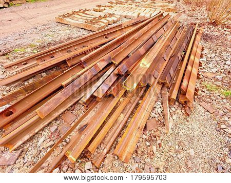 Heap of rusty rails in junkyard. Stock of steel rails from closed railway station. Metal material is waiting for transport to steel foundry for recycling