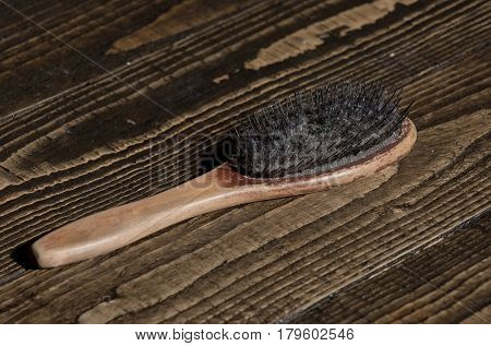 Old wooden hairbrush or paddle brush with dirty bristles for detangling and brushing on timber background. Hair loss problem