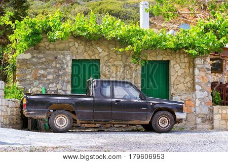 Bali Greece - April 30 2016: Old black pickup truck Mitsubishi L200 parked under a mountain in background of stone wall of the barn. Easy 4wd truck Japanese production. Resort village Bali Crete