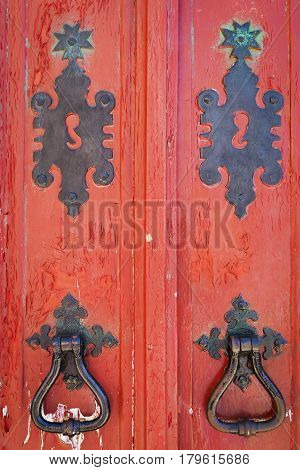 Detail of an old red wooden doors with black ironmongery
